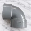 Elbow PVC 3 Inch Pralon warna abu-abu dengan logo Pralon di bagian sambungan, diletakkan di atas permukaan marmer