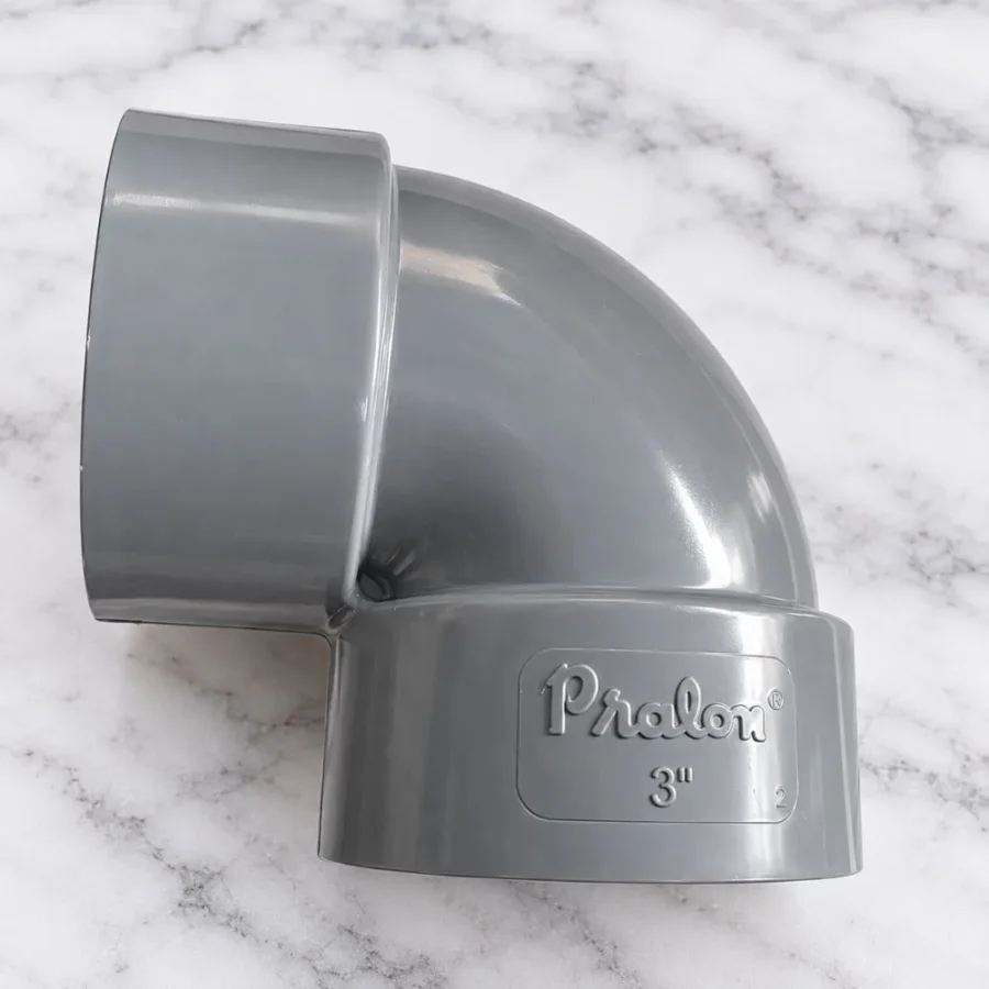 Elbow PVC 3 Inch Pralon warna abu-abu dengan logo Pralon di bagian sambungan, diletakkan di atas permukaan marmer